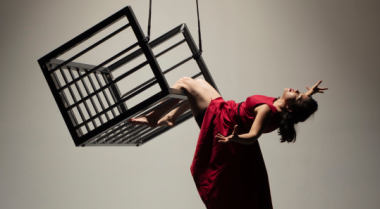 Female dancer in red dress hanging from cage