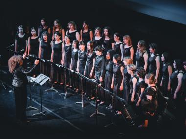 The San Francisco Girls Chorus on a dark stage, being conducted by Valérie Sainte-Agathe