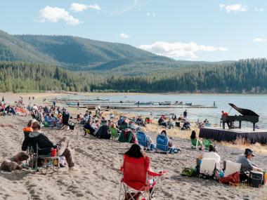 Hunter Noack plays a piano on a beach.  The audience is seated on blankets and camp chairs.