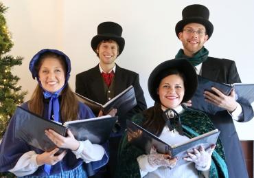 Four smiling Christmas carolers in Victorian costumes