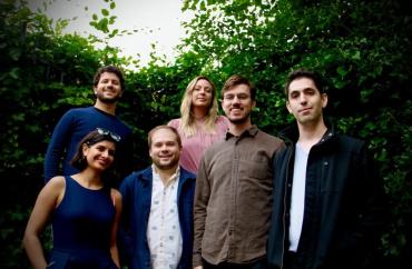 Six members of Ensemble Decipher standing in front of a large bush, smiling.
