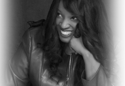 A black and white image of Nkeiru Okoye, smiling with her chin resting on her hand.