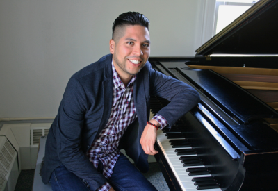Musician Erick Peralta smiles and leans over the keyboard of a grand piano