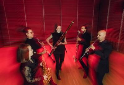 Five musicians playing reed instruments, blurred, in motion, in vivid red lighting