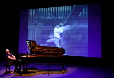 Adam Tendler playing piano in front of a projected image.