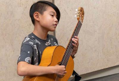 A Colburn Community School Suzuki guitar student holding a guitar.