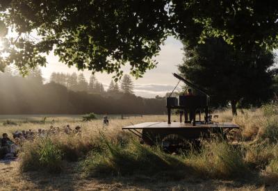 Hunter Noack plays piano in a field with audience members seated in camping chairs while the sun sets