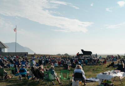 Hunter Noack plays piano in a field with audience members standing and seated in camping chairs