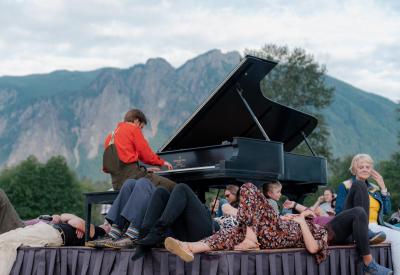 Hunter Noack plays the piano on a stage and audience members surround him and the piano listening to him play